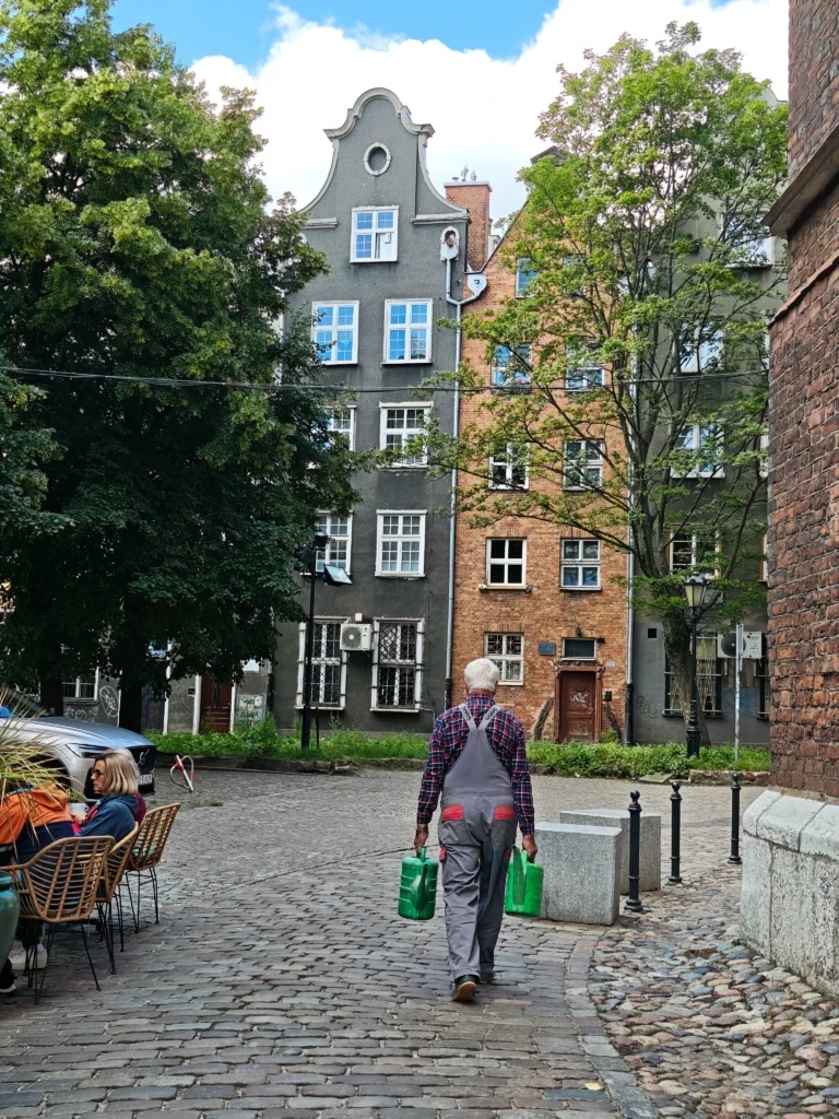 a local Pole holding two watering cans walking in a quiet residential neighbourhood of Gdansk, a hidden gem Polish city