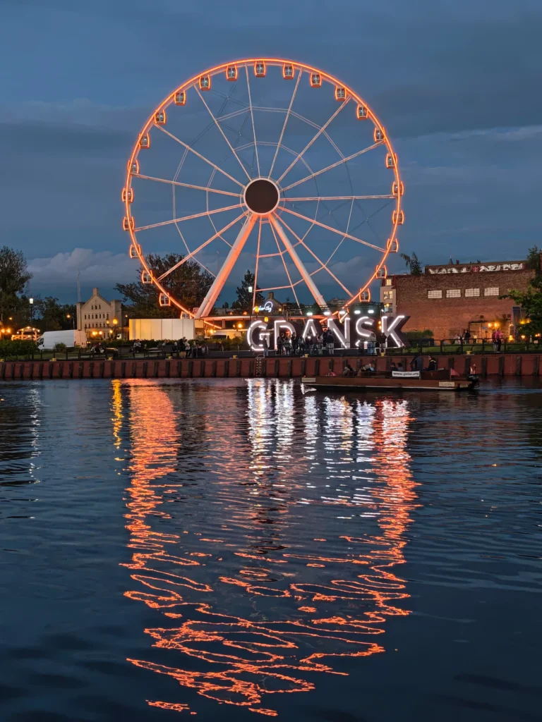 sign of the lit up glowing Gdansk sign at the harbourside, with a ferris wheel behind